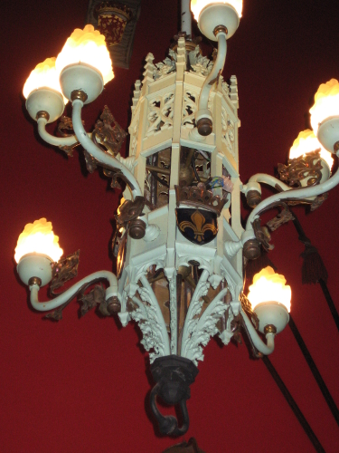 A metal chandelier decorated with fleur-de-lis and Scottish motifs.